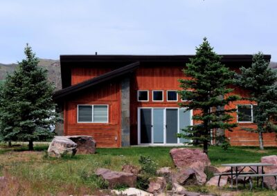 Luxury Mountain Cabin BackYard Showing Rock Garden, Large Green Grass Area, Cement Patio With BBQ. GLASS SLIDER DOOR entrance into stand-alone private family cabin.