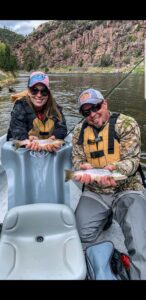 Husband and wife side by side in a green river fishing guide drift boat in Red Canyon releasing two wild brown trout into the green river by Dutch John resort