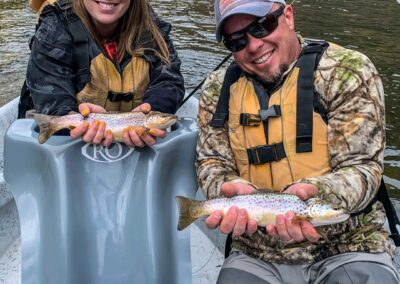 Husband and wife side by side in a green river fishing guide drift boat in Red Canyon releasing two wild brown trout into the green river by Dutch John resort